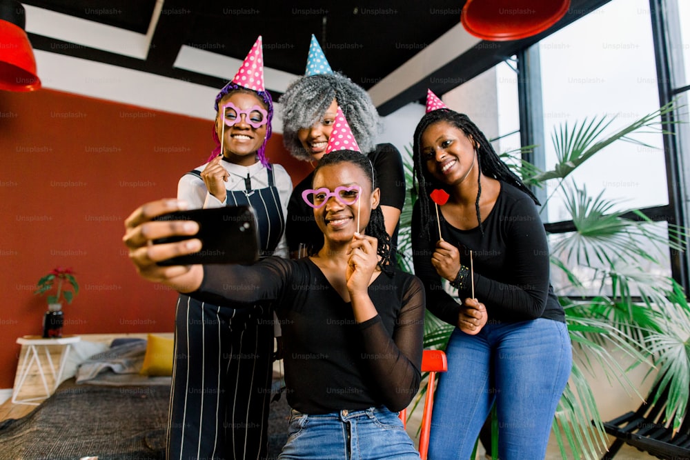 Happy african girls celebrate birthday in hats and take pictures on a smartphone