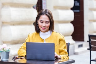 Bild einer glücklichen asiatischen Frau mit Laptop und Smartphone im Café. Junges, schönes Mädchen, das in einem Café sitzt und am Computer arbeitet