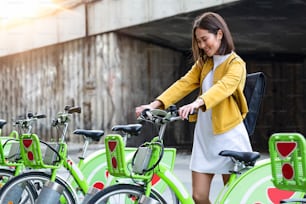 도시 자전거 - 공공 도시 자전거 공유 시스템을 사용하는 아시아 여성. 도시 자전거로 자전거를 탄 후 여성 전문 주차 도시 자전거를 자전거로 타고 있습니다.