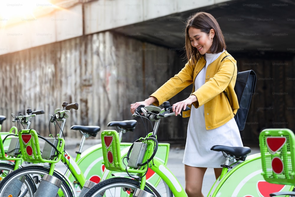 City bike - Asian woman using public city bicycles sharing system. Biking female professional parking city bikes after cycling on city bicycle.