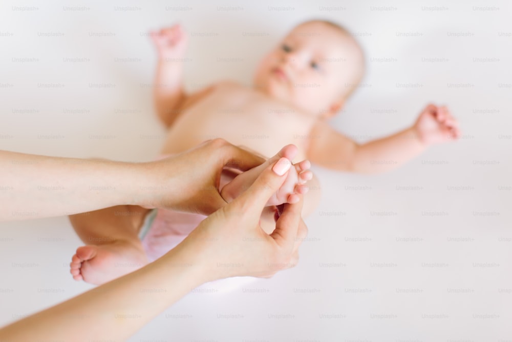 白い背景に赤ちゃんの足をマッサージする母の手。