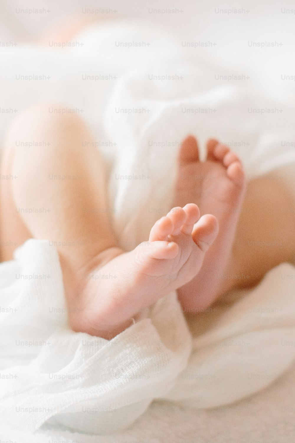 Pernas do bebê pequeno recém-nascido no pano peludo vestindo a faixa branca da cabeça