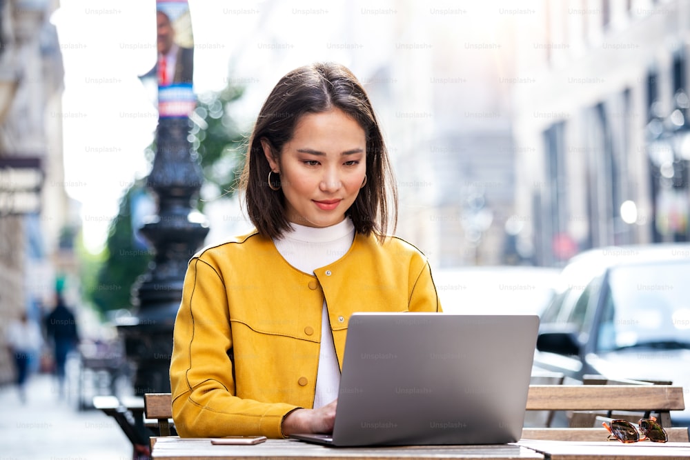 Asian Woman working on laptop at a cafe. Young woman working on a laptop. Beautiful young woman working with laptop from coffee shop. Attractive woman sitting in a cafe with a laptop
