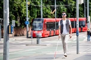 Young blind man with white cane walking across the street in city. Copy space.
