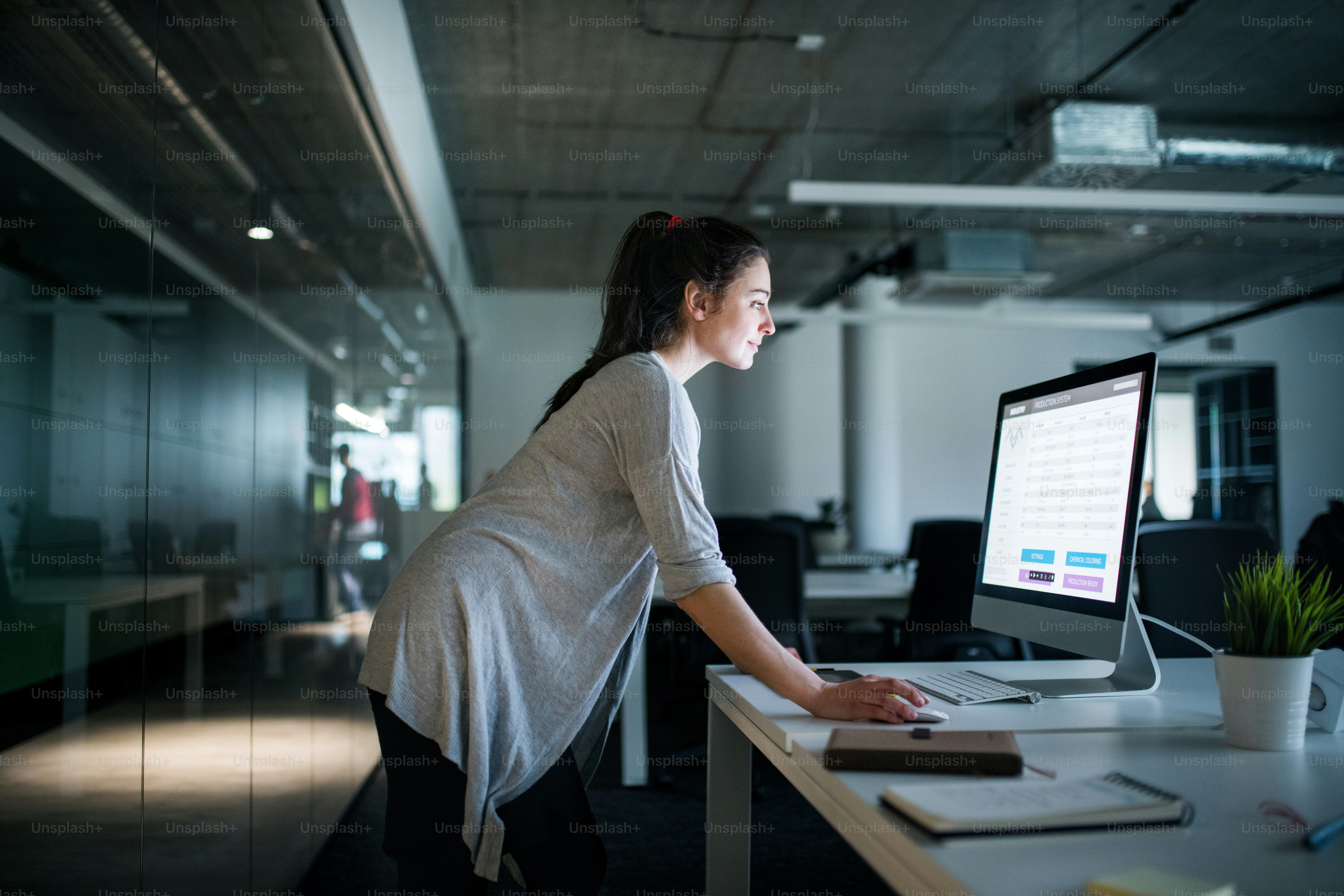 Side view of young businesswoman with computer standing at the desk in an office, working.