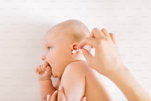 Mother hand cleaning baby ear with cotton swab.