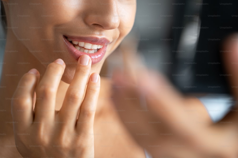 Foto cortada de uma jovem mulher caucasiana sorridente colocando um bálsamo labial