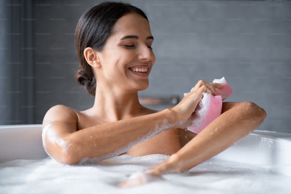Mujer joven sonriente lavando el brazo con una esponja