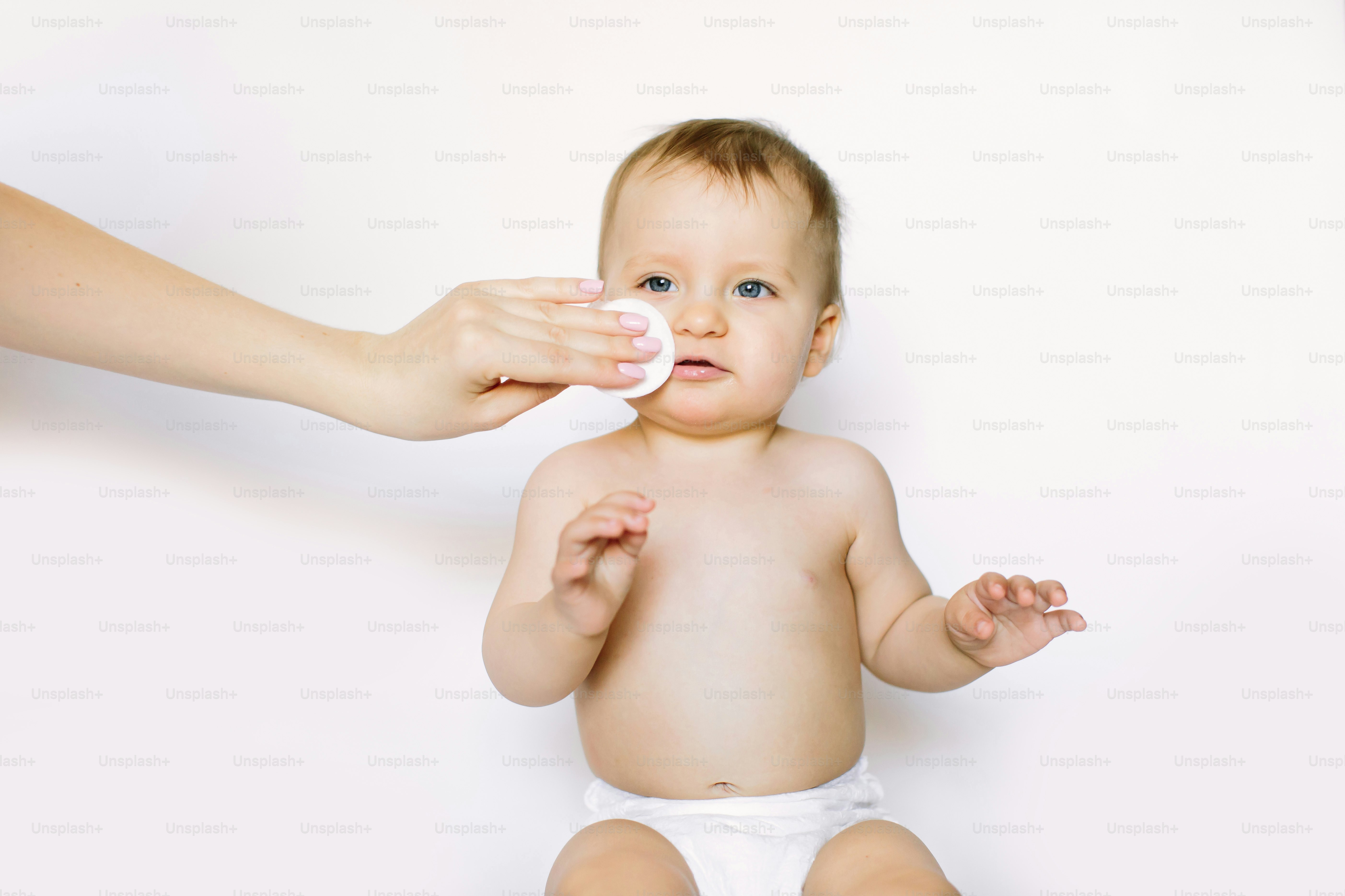 Mother cleaning eyes of a newborn baby with physiological solution on a cotton disk.