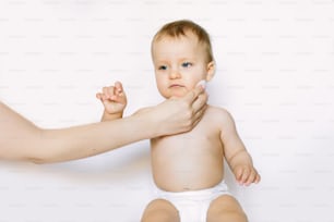 Junge Mutter wischt den Körper und das Gesicht der Babyhaut mit feuchten Tüchern sorgfältig auf weißem Hintergrund ab. Konzept Reinigungstuch, rein, sauber.