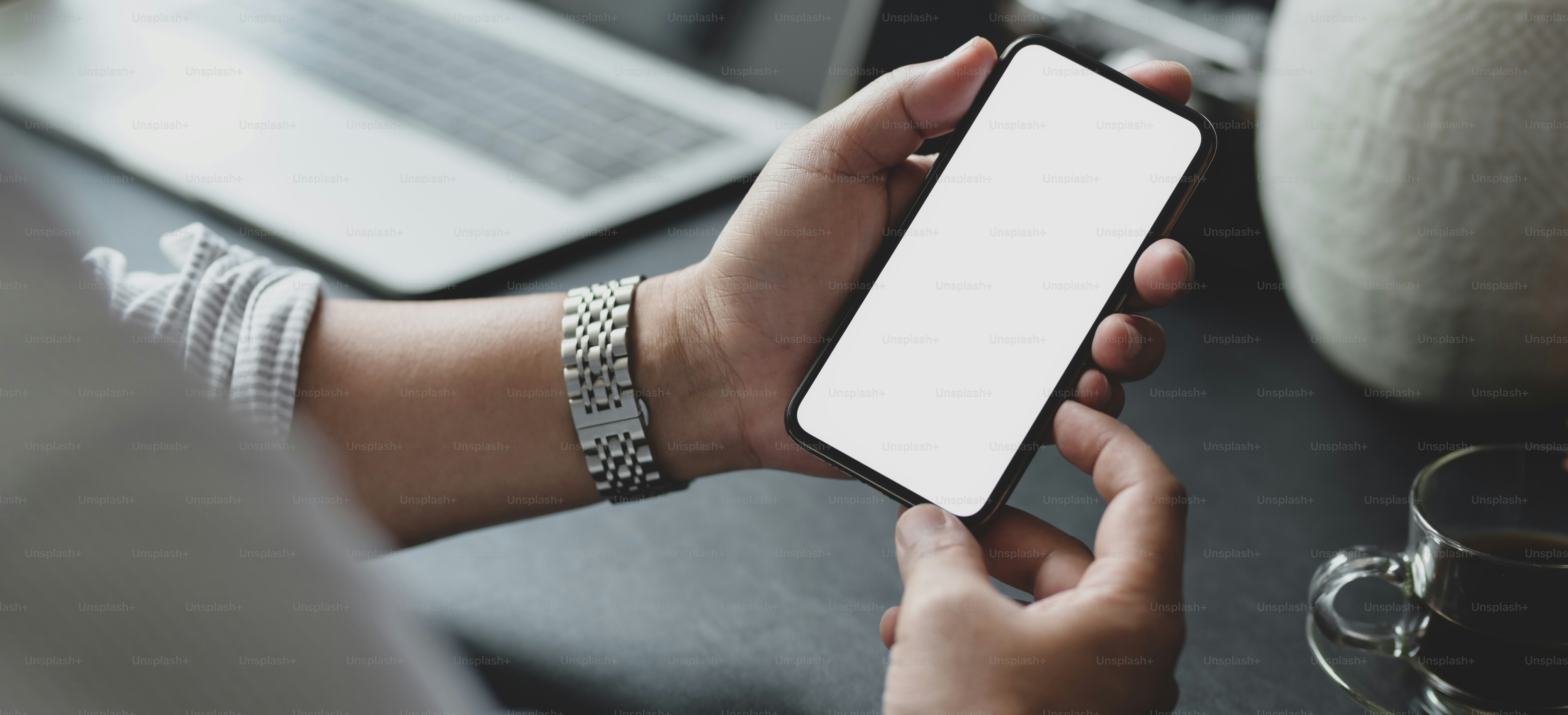 Close-up view of businessman holding blank screen smartphone in his modern office room while working on his project