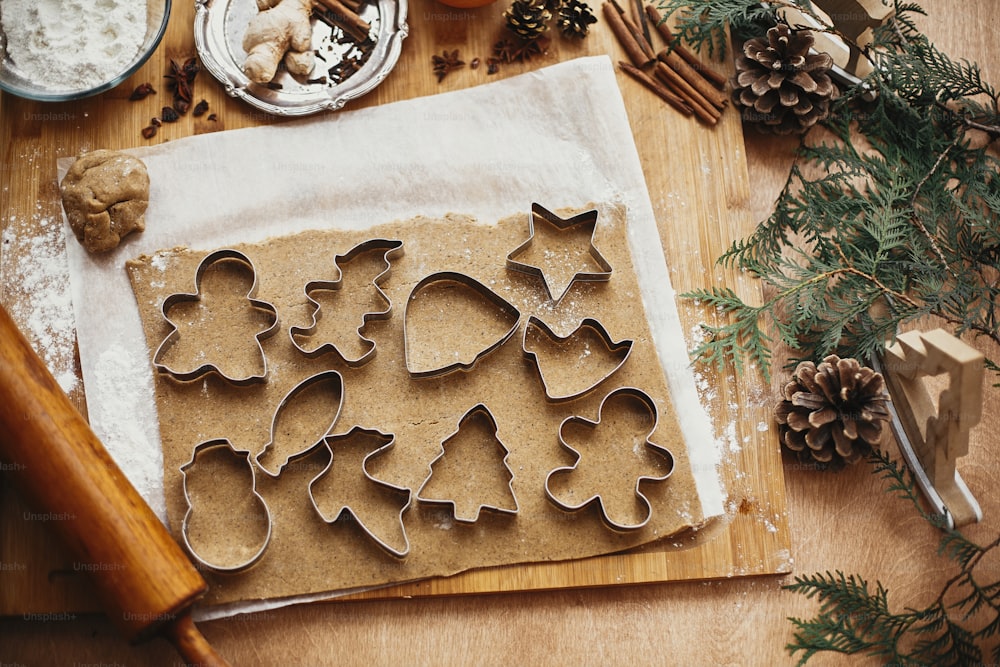 Preparare i biscotti di pan di zenzero di Natale, flat lay. Pasta cruda con tagliapasta in metallo per biscotti e mattarello in legno, anice, zenzero, cannella, pigne, rami di abete su tavolo rustico.