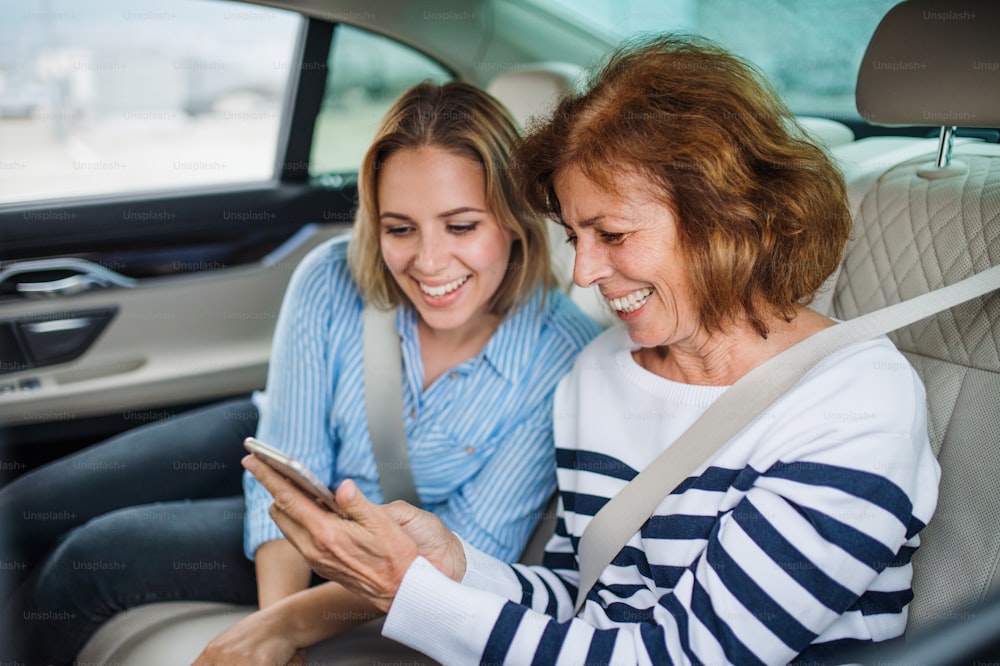 Two cheerful adults sitting on back seats in car, using smartphone.