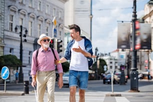 A young man and blind senior with white cane walking in city, crossing street.