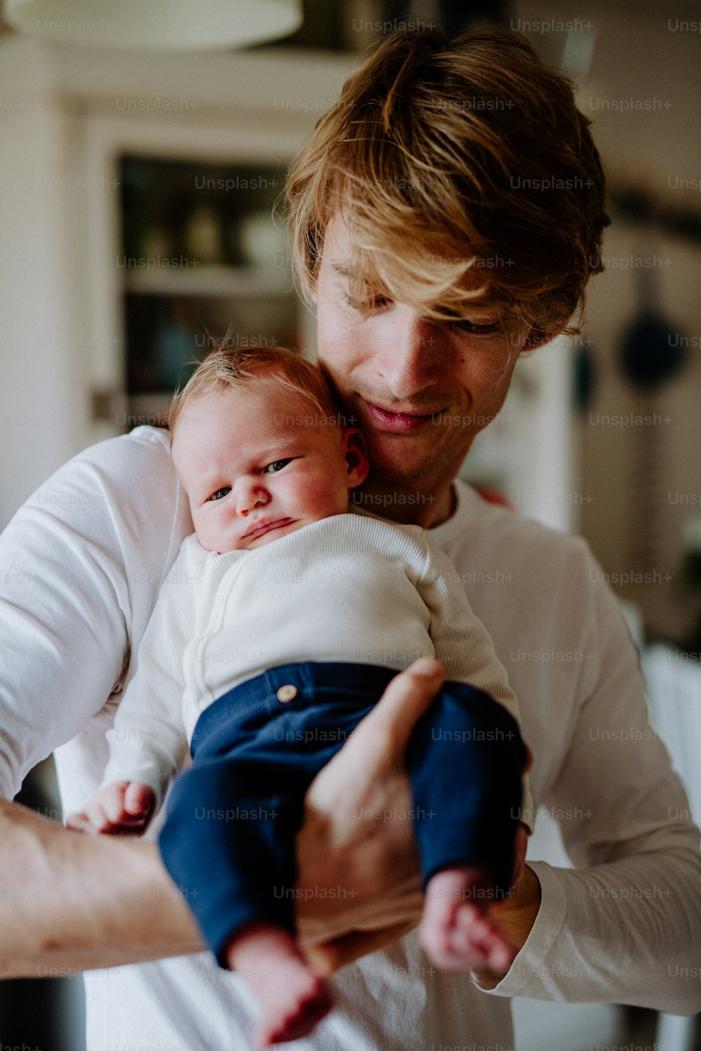 A young father holding a newborn baby at home, front view.