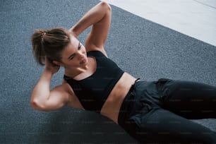 In schwarzer Kleidung. Bauchmuskeln auf dem Boden im Fitnessstudio machen. Schöne weibliche Fitnessfrau.