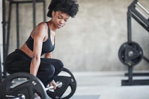 Lifting exercises. African american woman with curly hair and in sportive clothes have fitness day in the gym.