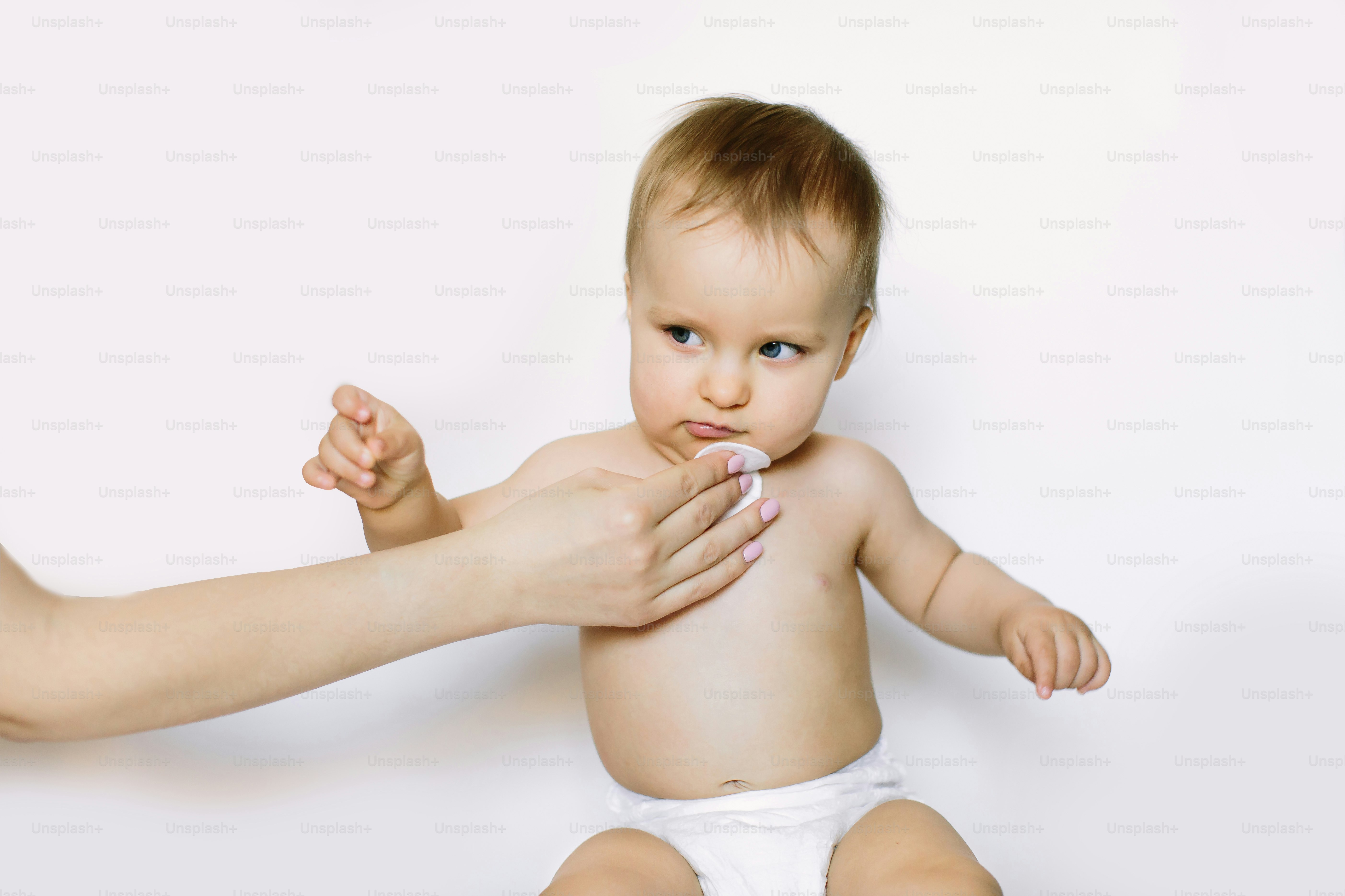 Young mom wiping the baby skin body and face with wet wipes carefully on white background. concept cleaning wipe, pure, clean.