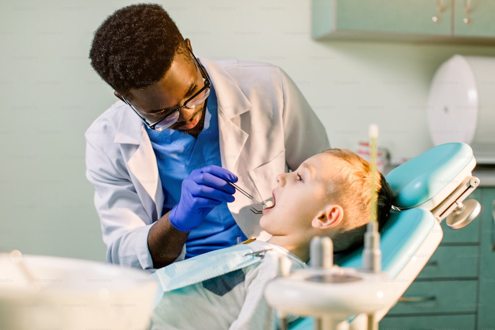 Children's dentistry, Pediatric Dentistry. A male African-American stomatologist is treating teeth of a school-age boy. Oral health and hygiene