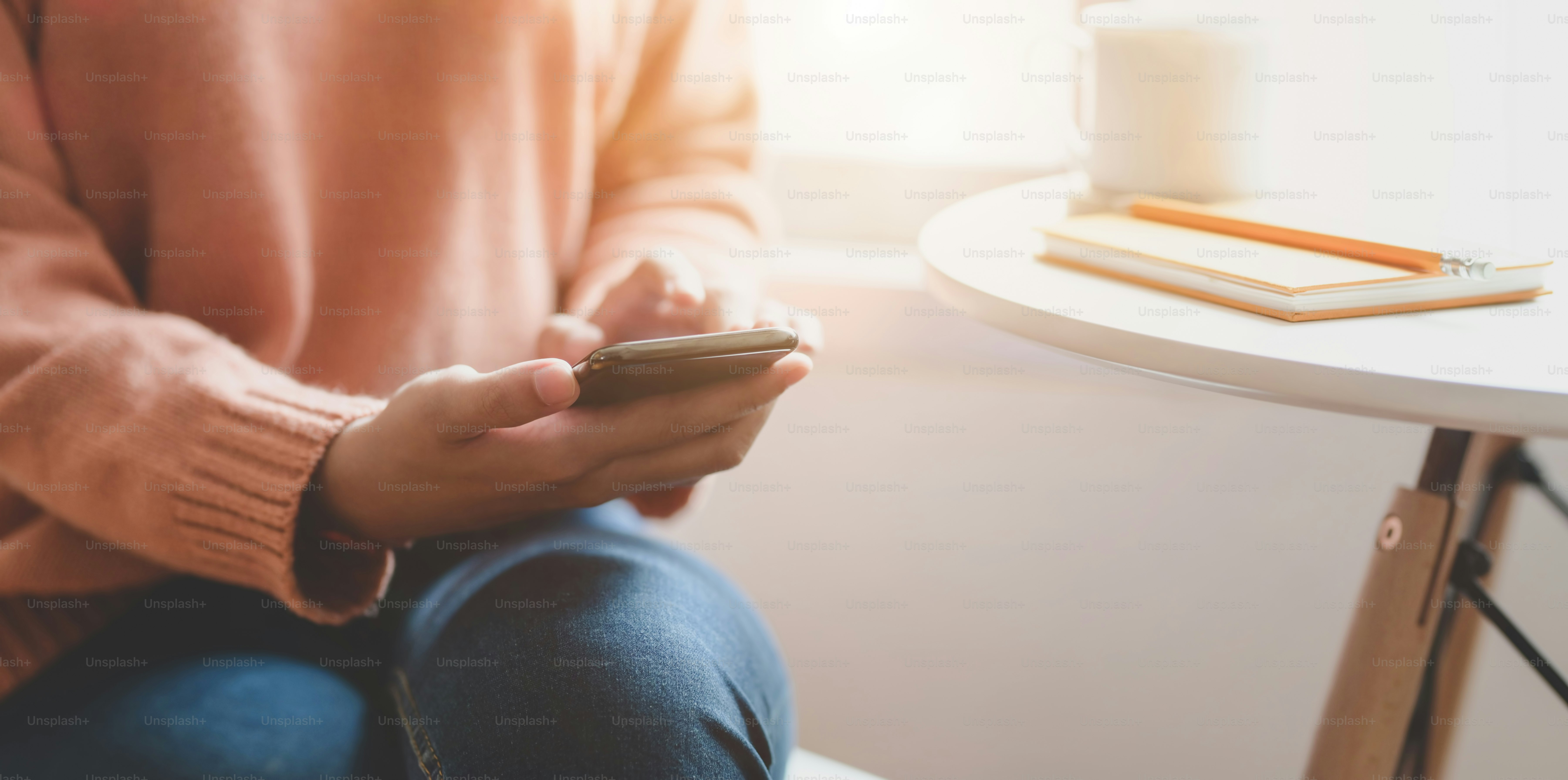 Cropped shot of young female holding smartphone in comfortable workplace near the windows