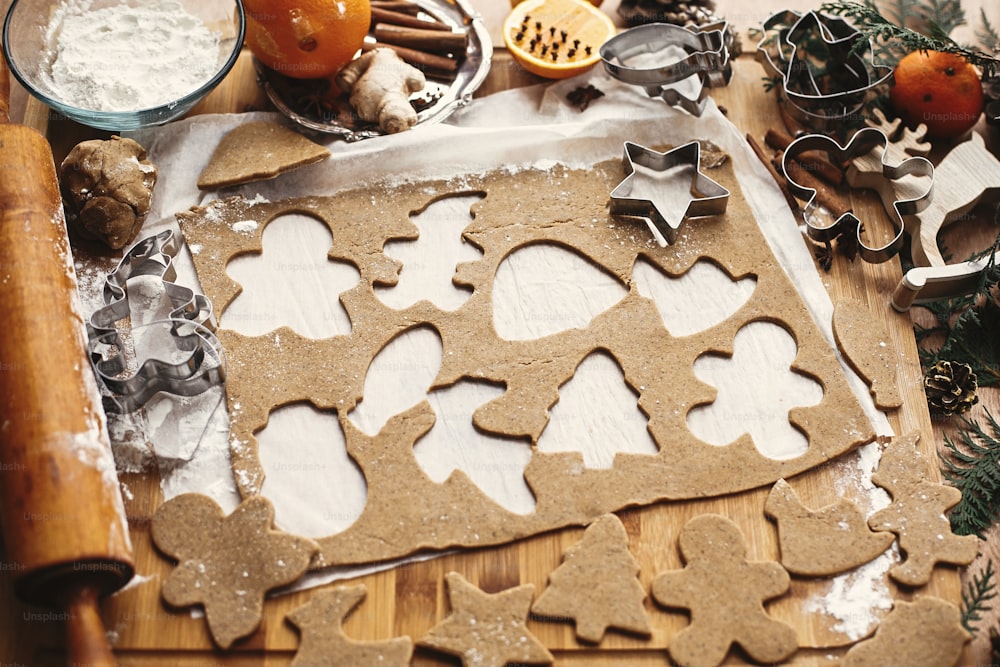 Gingerbread dough with metal cutters in different shapes for christmas cookies and wooden rolling pin, anise, ginger, cinnamon, pine cones, fir branches, flour on rustic table