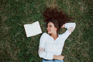Young writter. Girl lying down on the green grass and have a rest.