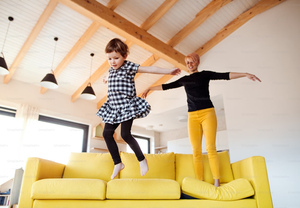 A young woman with small daughter jumping on a sofa at home, having fun.