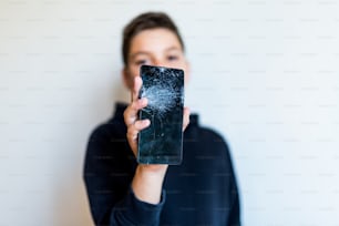 Broken glass screen smartphone in hand of upset boy, white background. Worried kid Holding Broken Smartphone At Home