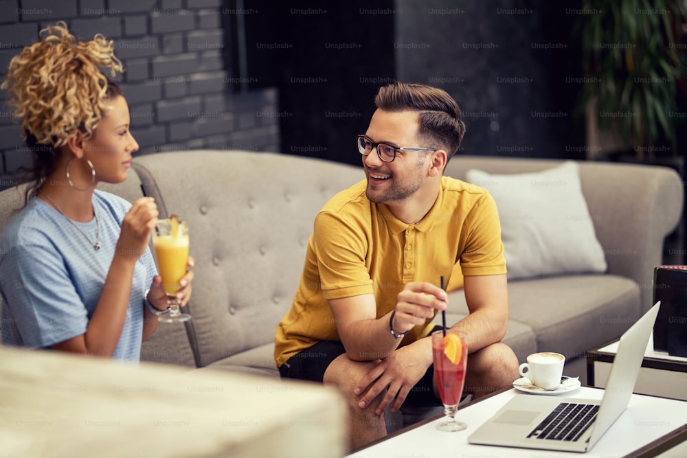 Hombre feliz y su novia bebiendo cócteles de frutas y hablando mientras están sentados en un café.