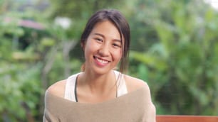 Asian woman feeling happy smiling and looking to camera while relax on table in garden at home in the morning. Lifestyle women relax at home concept.