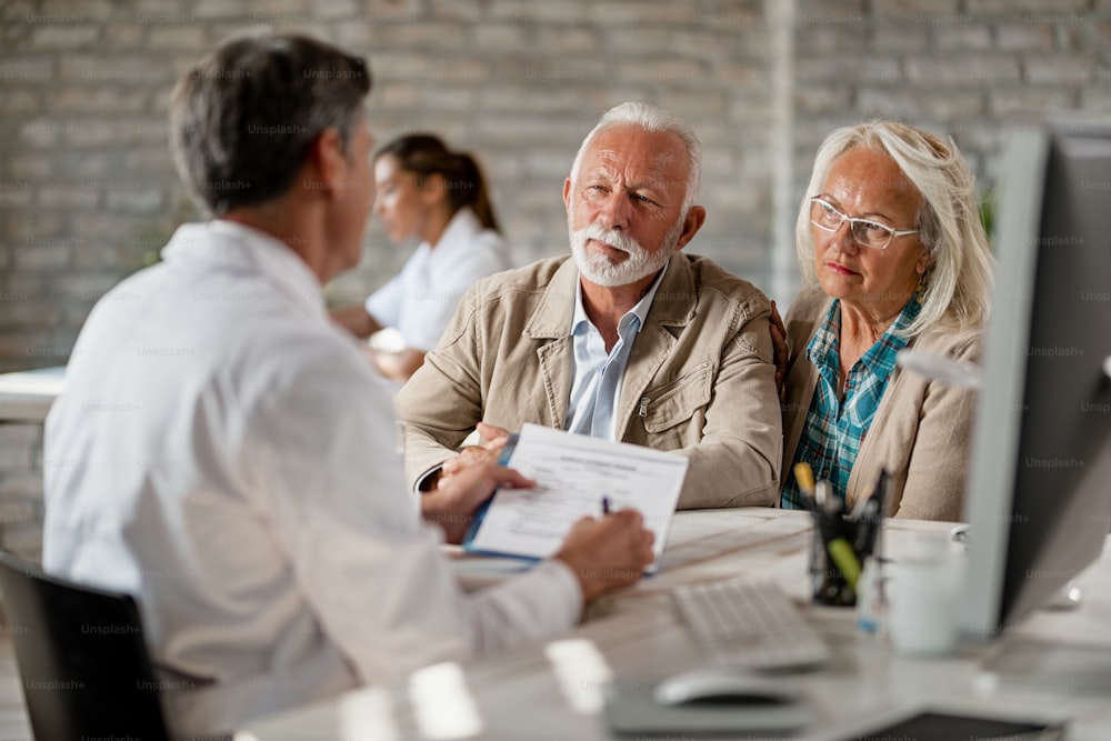 Coppia anziana che si consulta con l'operatore sanitario sulla loro polizza assicurativa durante un incontro in clinica.