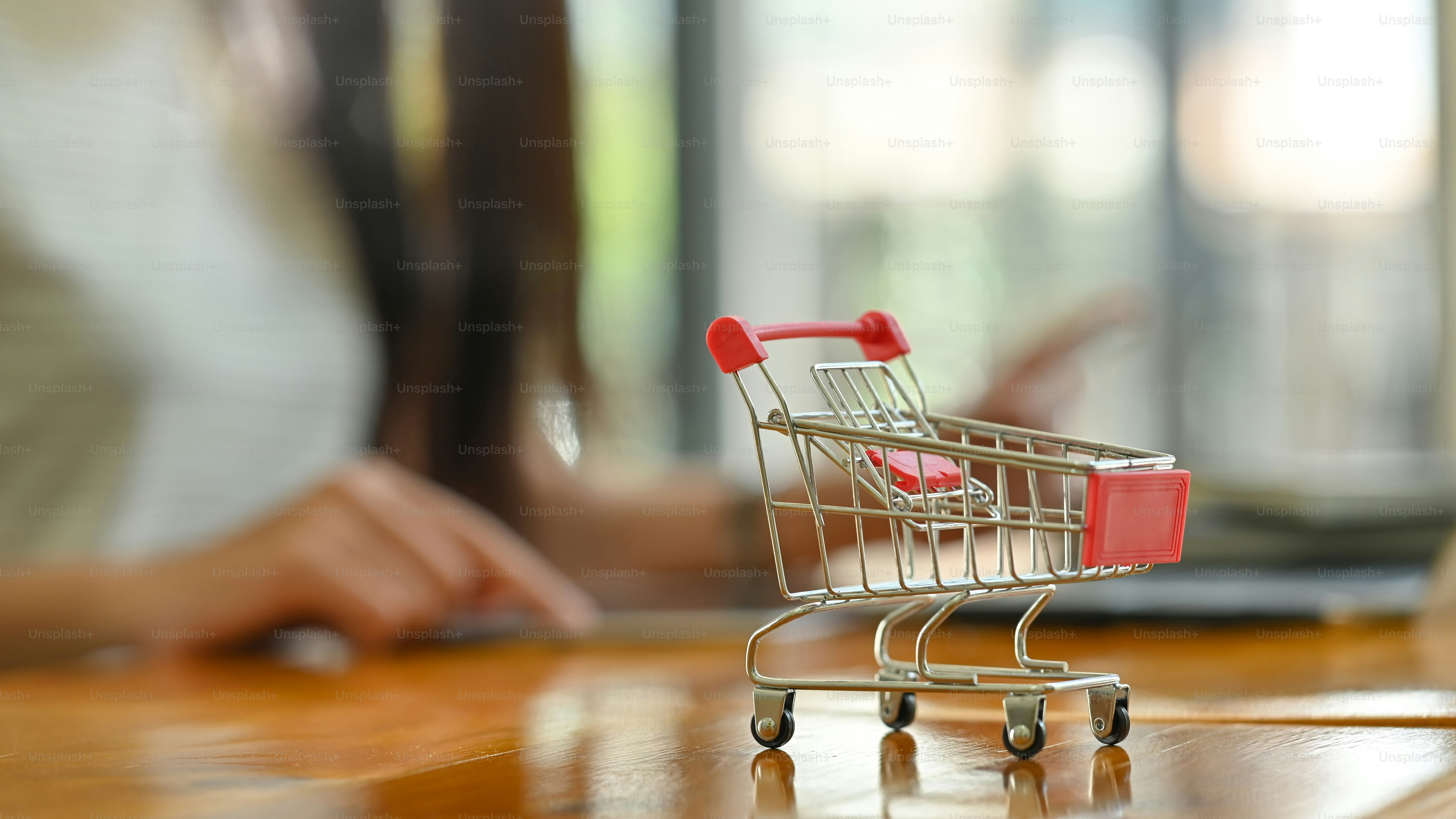Panier de chariot mis sur le bois avec femme faisant des achats en ligne en arrière-plan flou.