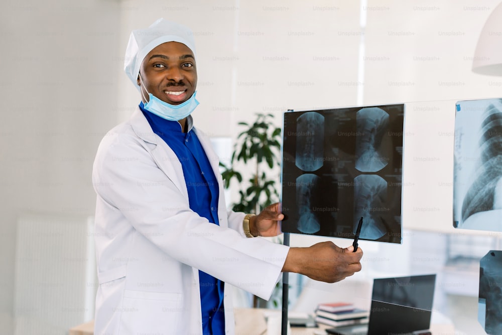 Concepto de consultorio médico y práctica médica. Médico afroamericano sonriente profesional en la clínica señalando en rayos X