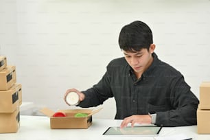 若い男のオンライン中小企業の所有者は、箱にドロップ製品を梱包します。