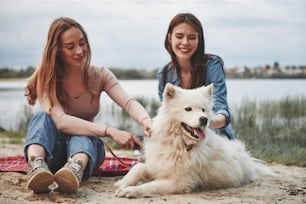 두 여자 친구는 귀여운 강아지와 함께 해변에서 즐거운 시간을 보냅니다.