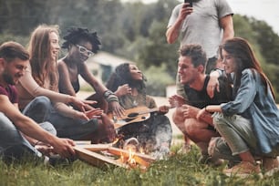 Rest near campfire. Group of people have picnic on the beach. Friends have fun at weekend time.