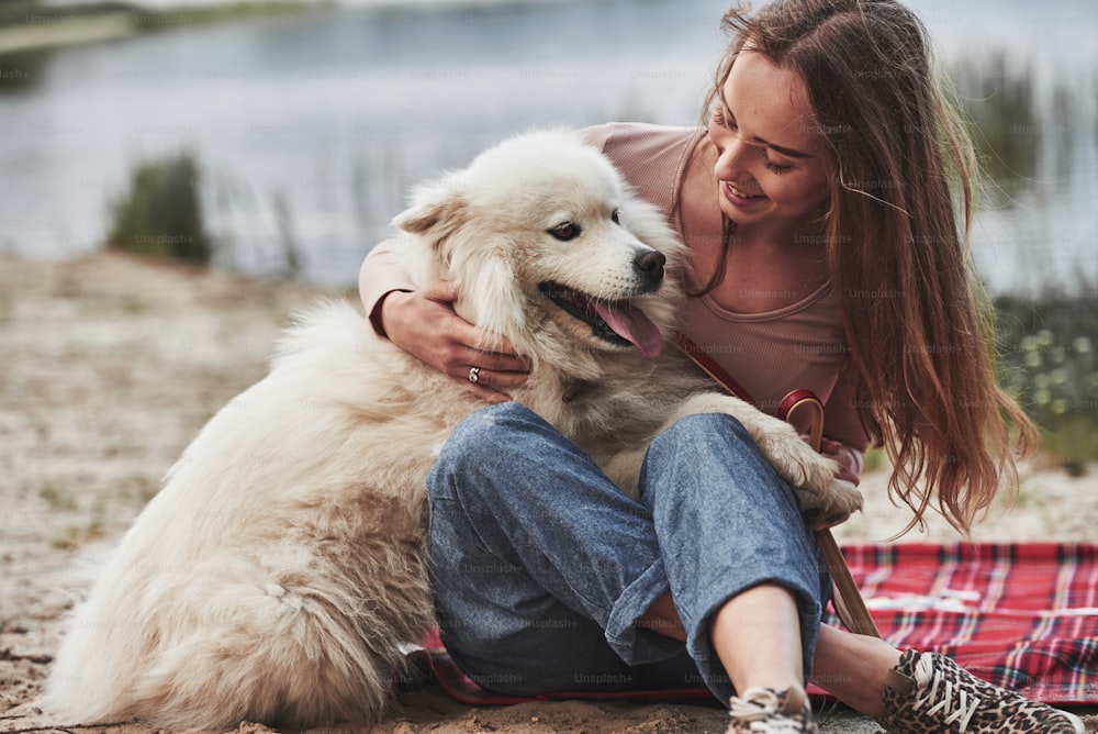 Blurred background. Blonde girl with her cute white dog have a great time spending on a beach.