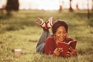 Completamente concentrato sulla lettura di libri interessanti. Allegra donna afroamericana nel parco in estate.