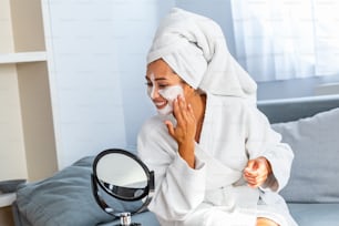 Young beautiful woman applying homemade facial mask i at home.Skin care, beauty treatments. So beautiful. Close-up of girl with beauty mask on her face looking in mirror.