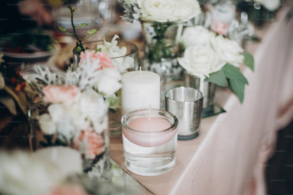 Candle, White  flowers in modern glass vase on pink centerpiece. Stylish luxury decor on wedding table.Luxury catering and adorning. Holiday feast