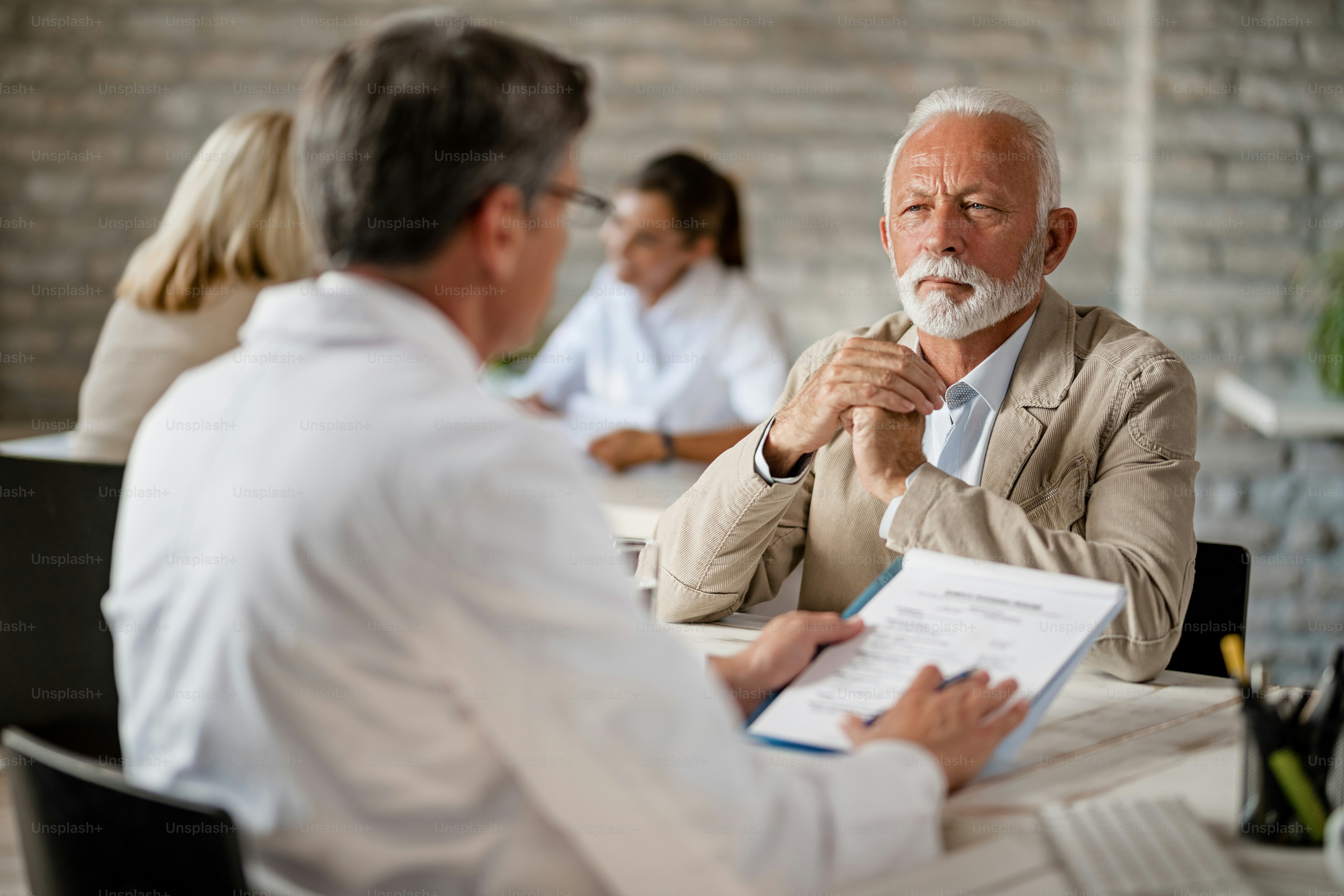 Senior man and healthcare worker communicating about medical insurance documents during a meeting at clinic.