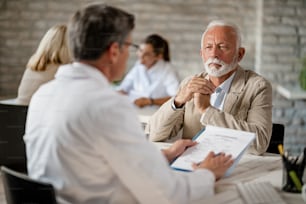 Homem sênior e profissional de saúde se comunicando sobre documentos de seguro médico durante uma reunião na clínica.
