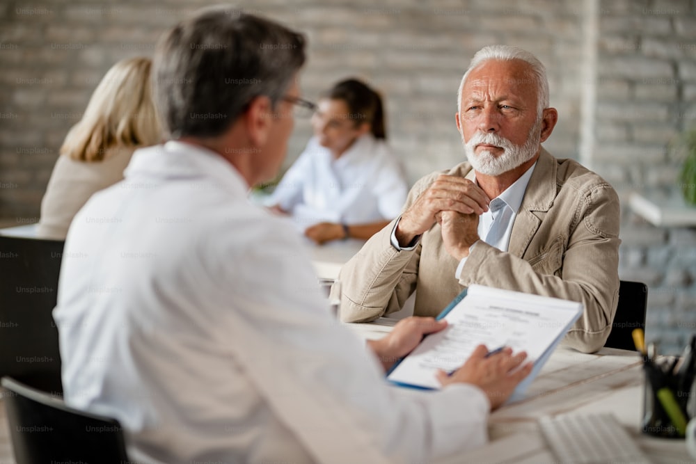 Senior man and healthcare worker communicating about medical insurance documents during a meeting at clinic.