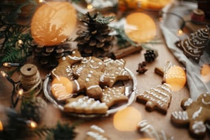 Biscoitos de gengibre de Natal no prato vintage e anis, canela, pinhas, ramos de cedro com luzes douradas na mesa rústica. Homem de gengibre tradicional assado, árvore, biscoitos estrela