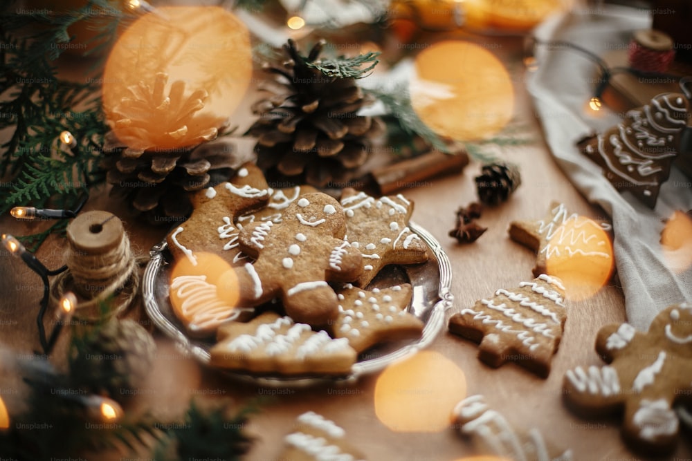 Weihnachtslebkuchenplätzchen auf Vintage-Teller und Anis, Zimt, Tannenzapfen, Zedernzweige mit goldenen Lichtern auf rustikalem Tisch. Gebackener traditioneller Lebkuchenmann, Baum, Sternkekse