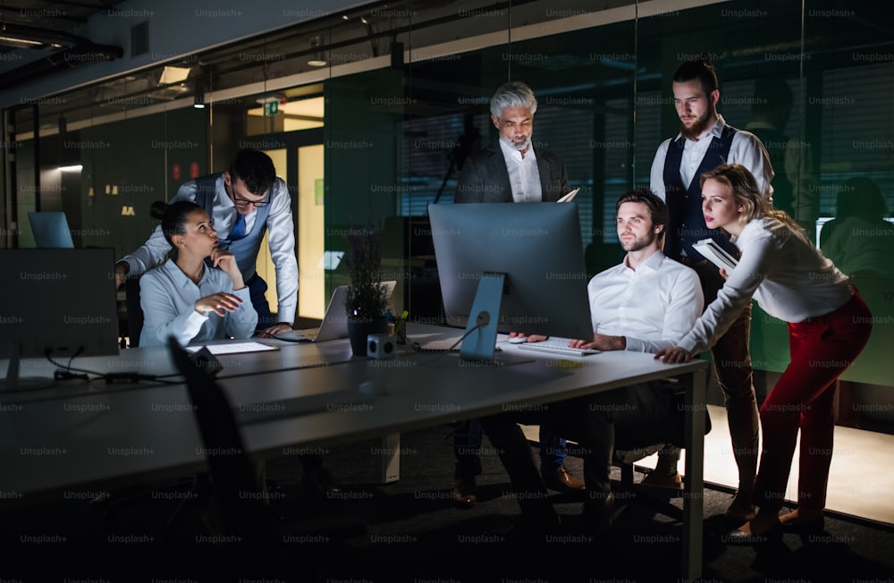 Un gruppo di uomini d'affari in un ufficio di sera o di notte, usando il computer.