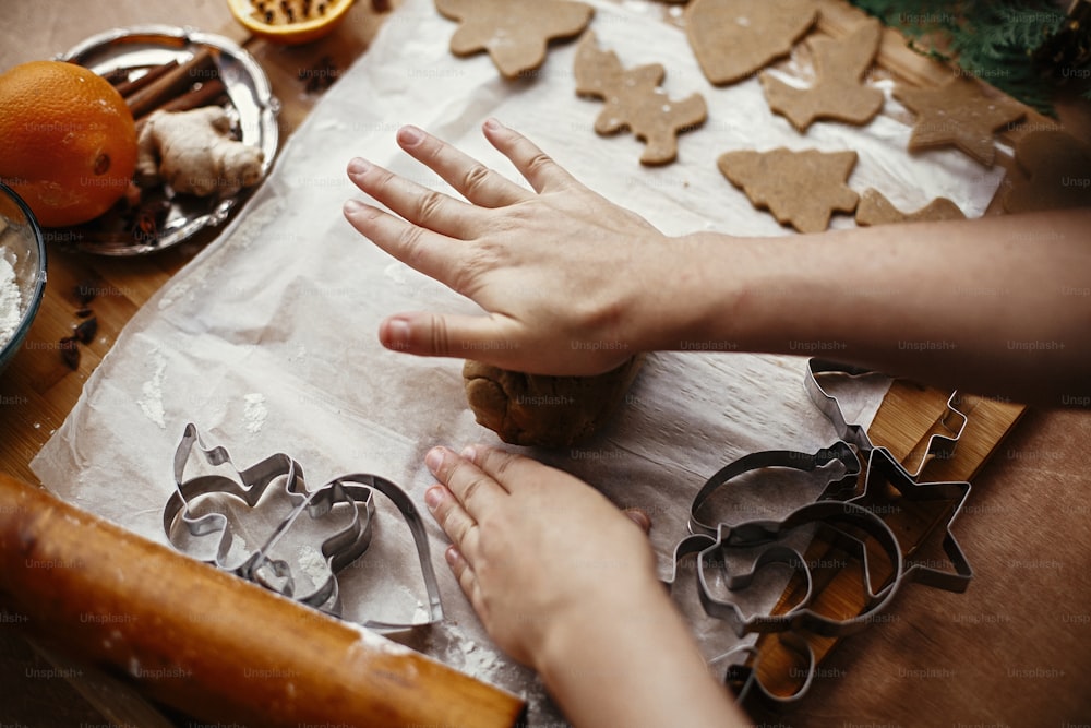 Hands kneading raw dough on background of rolling pin,metal cutters, anise, ginger, cinnamon, pine cones, fir branches on rustic table.Making christmas gingerbread cookies.