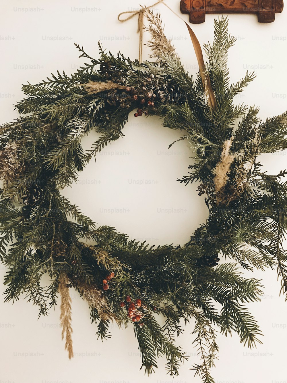 Stylish rustic wreath on white wall. Rural modern wreath hanging white wall background in room. Happy Holidays. Festive decoration. Phone photo