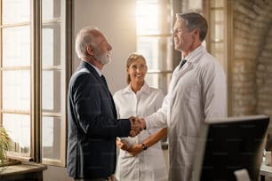 Happy doctor shaking hands with senior businessman while nurse is standing in the background.
