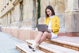 노트북 컴퓨터를 사용하는 아름다운 아시아 여성. 웃는 아시아 소녀는 계단에 앉아 노트북을 사용하고 있다. 노트북 컴퓨터를 사용하는 아시아 비즈니스 여성